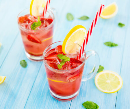Colorful refreshing drinks for summer, cold strawberry lemonade juice with ice cubes in the glasses garnished with sliced fresh lemons
