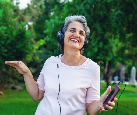 Senior woman listening music with headphones in the park