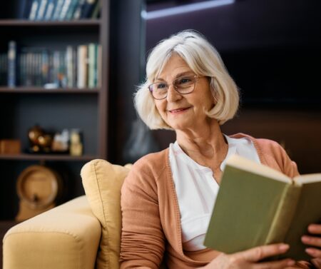 Happy,Senior,Woman,Enjoying,While,Reading,Book,In,Living,Room